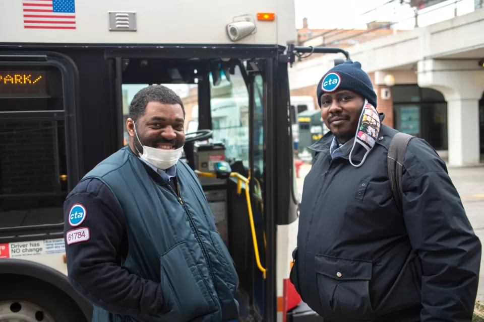 Two Chicago transit operators standing in front of a bus and smiling at the camera